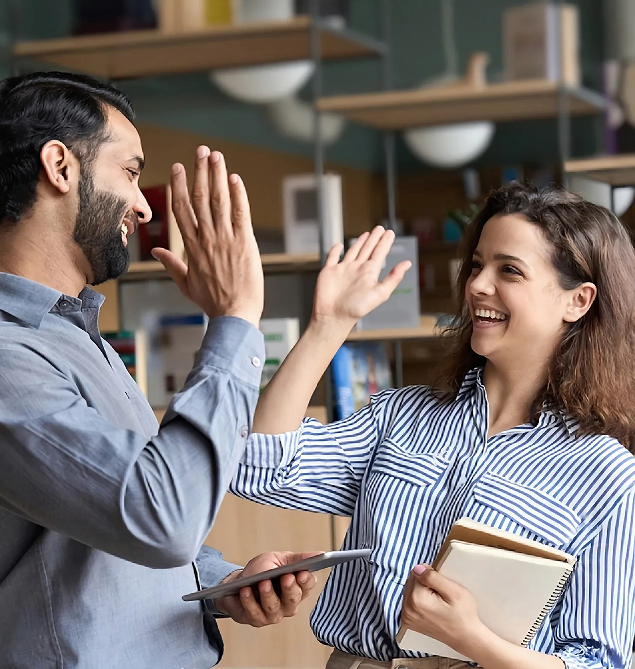 Two friendly cheerful diverse professionals, teacher and student high-fiving in the office celebrating success, good collaboration result, partnership teamwork, and team motivation at office work.